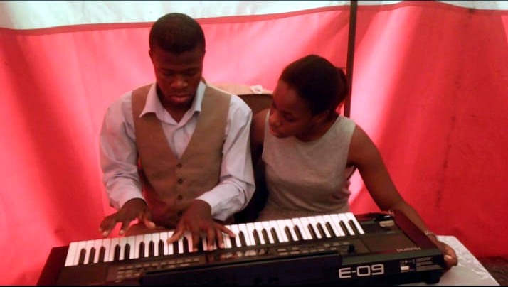 A young person playing a keyboard with a mentor